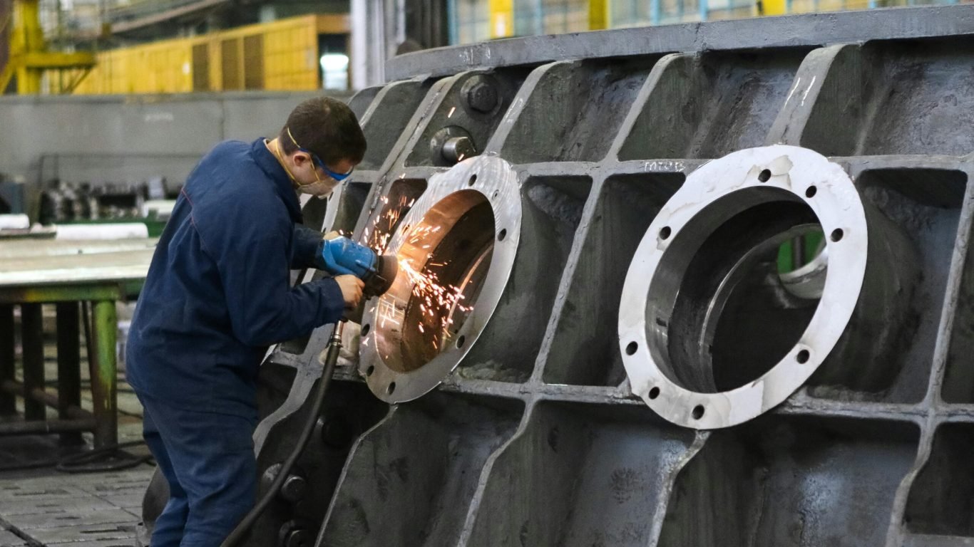 pexels-photo-2965260-2965260 A worker in protective gear grinding metal, creating sparks in a factory setting.